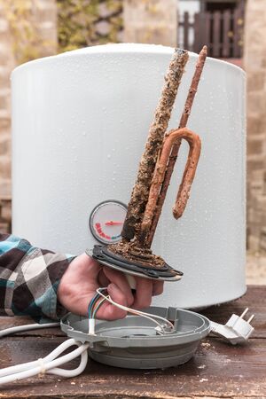 men's hand holding heating element for water heating tank.