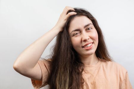 Dandruff and lice. Portrait of a young Caucasian brunette woman in a beige t-shirt, who strongly...
