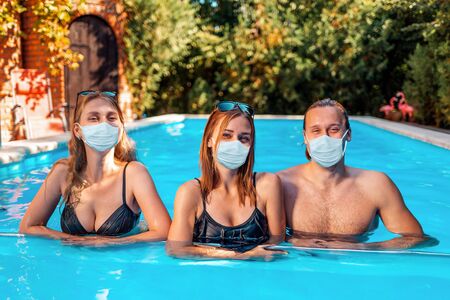 A holiday at sea and protection from viruses. A group of young people pose in a pool with medical masks on their faces. The concept of self-isolation and pandemics.の写真素材