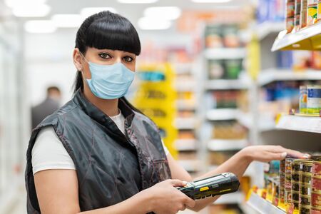 Coronavirus. A store clerk in a medical mask checks the product on the shelves using an electronic...