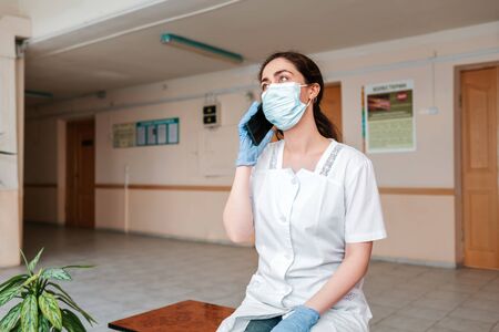 Coronavirus.A doctor in a lab coat, medical mask and gloves, sitting resting in the corridor and...