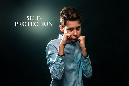 The concept of domestic violence. The boy folded his fists and defends himself against aggression. Black background. Text Self-protection .の写真素材