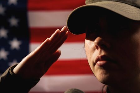 Memorial day. A female soldier in uniform salutes against the background of the American flag. Close-up portrait. The concept of the American national holidays and patriotism.