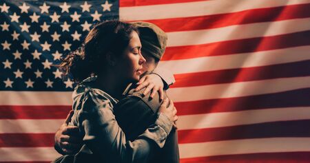 Independence day, memorial Day. A woman embraces a soldier. Couple on the background of the American flag. Copy space. The concept of American national holidays and patriotism.の写真素材