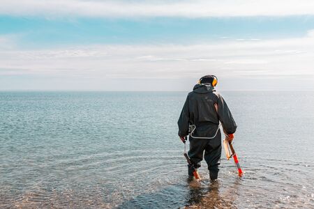 A man standing knee-deep in the water looking for precious metals with a metal detector. Sea and sky on the background.の写真素材