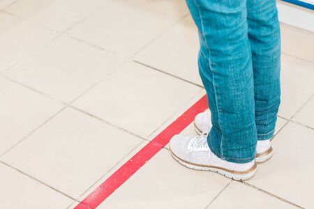 Person stand in line, legs close-up. Attention line on the floor of the store to maintain social distance. Concept of the coronavirus pandemic and prevention measures.の写真素材