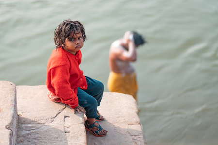 December 17 2019 Varanasi, India. Portrait of a bored child sitting on the steps near the river. In...