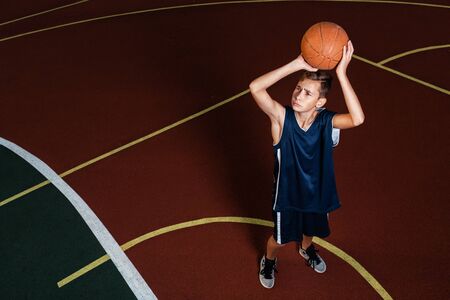 Sports and basketball. A young teenager in a blue tracksuit throws a jump ball into the basket....