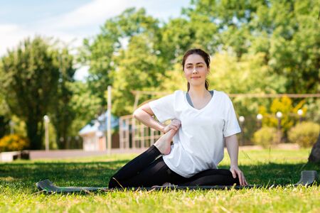 Yoga. A smiling young woman in sports clothes, doing an exercise in the Park on the grass. Side...