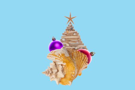 Collage of modern art. The concept of new year holidays at the resort. Large sea shell on which there is a Christmas tree crafts from shells and branches with Christmas toys. Blue background.の写真素材