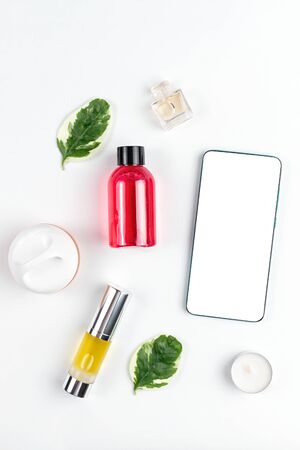 Cosmetics. On a white background are shower gel, oil in a tube, candle, cream and perfume, next to the phone. Flat lay. Mock up. Concept of modern technology and beauty.の写真素材