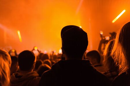 A crowd of people at the concert have fun and dance to the music at the concert. Orange light in the background. Rear view. The concept of entertainment and relaxation.の写真素材