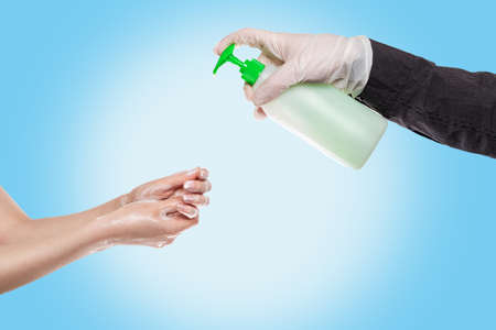 Hand washing.A man in medical gloves squeezes liquid soap on the hands of a woman who washes them with foam.Hands close-up.Blue background.Concept of antiseptic hand washing, disinfection and protection from bacteria and viruses.の写真素材