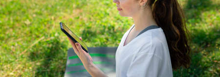 Close up portrait of a young smiling woman sitting on green grass and using a cellphone. Copy space....