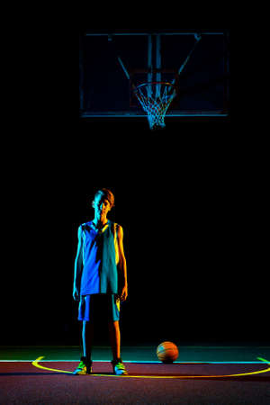 Basketball A teenage boy in green sportswear plays a basketball. In the background is a sports field. Copy space. Concept of sports games.の写真素材