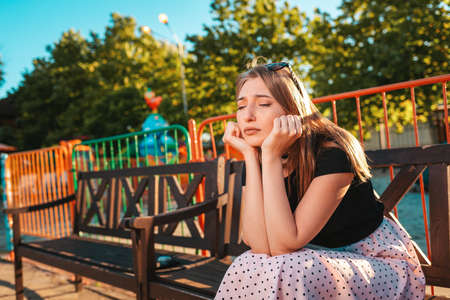 Sad emotions. A sad woman sits on a Park bench with her chin in her hands. The concept of human emotions.の写真素材