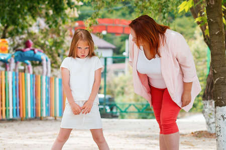 Family. The mother leans over to her daughter to understand why the girl is sad and Moody. There is a Playground in the background. Concept of education and upbringing.の写真素材