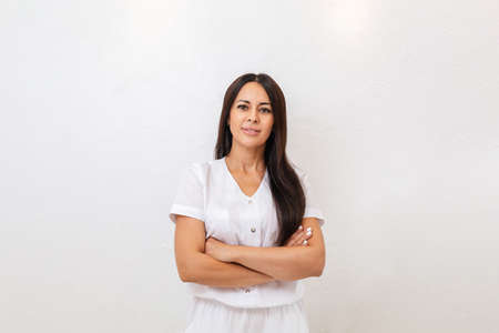 A tanned, pretty woman smiles and poses with her arms crossed. White background. Copy space. Concept...