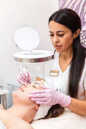 Beauty salon. The cosmetologist in rubber gloves makes mechanical cleaning of the client's face. Vertical. Concept of professional cosmetology and beauty.の写真素材