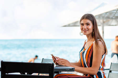 Portrait of a smiling woman sits in a cafe and uses a mobile phone. Concept of communication and...
