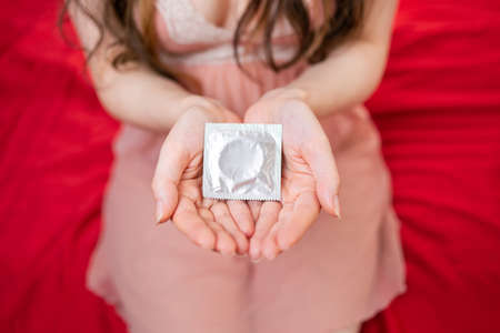World sexual health day. A woman in her underwear is sitting on the bed and holding a condom package in her hands. The view from the top. The concept of contraception and protection from AIDS.の写真素材