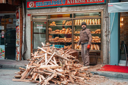 12/23/2019, Istanbul, Turkey. A man stands on the street next to a pile of firewood. In the background is the storefront of a bakery with bread.のeditorial素材