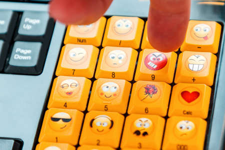 A finger presses a button on the keyboard with an angry emoji. Close up. Concept of social networks, communication and emotions.の写真素材
