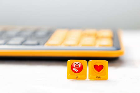 Two buttons with the image of an angry emoticon and a heart on the background of a blurred keyboard. The concept of social networks, communication and emotions.の写真素材