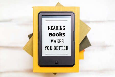 Reading and knowledge. E-book reader is on top of a stack of books on a wooden background. Flat lay....