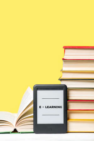 E-learning. E-book reader and a stack of books on a yellow background. Vertical. Copy space. Concept...