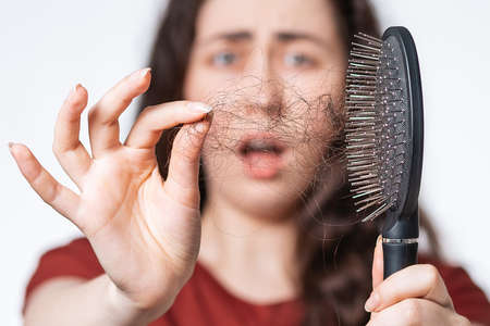 Close up portrait in a blur, a screaming brunette woman holds a comb in front of her, clearing it from a pile of fallen hair. White background. Concept of hair loss, baldness and hair care.の写真素材