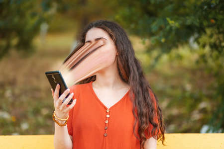 Portrait of a young long-haired woman using a smartphone. The face is smeared, sucked into the...