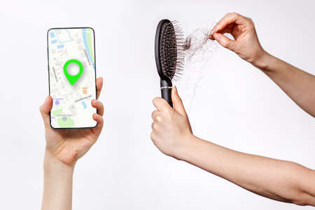 Females hands clean the comb from fallen hair, and holds a smartphone with an online maps app. White...