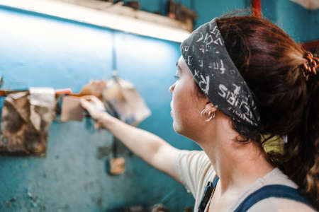 Gender equality. Portrait of a young woman in uniform working in a workshop, which attaches a piece of paper with a record on the wall. Background is blur. Close up.の写真素材
