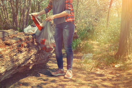 A volunteer cleans garbage in the forest after a season of picnics and barbecues. Tint and light. Eco.の写真素材