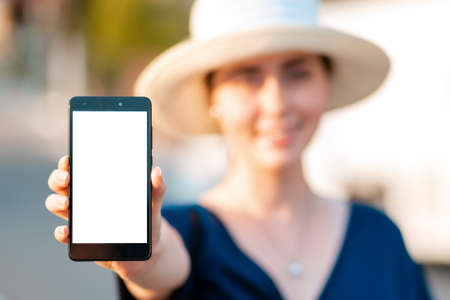 A woman in straw hat holds a smartphone in her hand, hand close-up. Portrait in a blur. Concept of modern technologies, business and applications for the phone.の写真素材