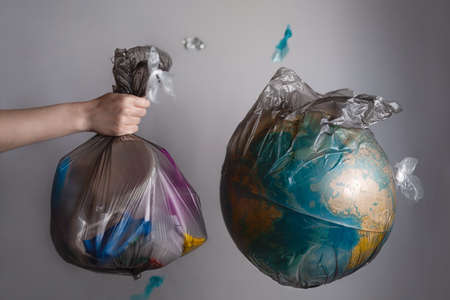 A woman's hand holds a garbage bag next to the globe of planet Earth. Concept of ecology and...