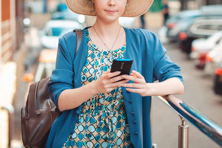 Close up portrait of elegant woman in a hat is typing something on her smartphone. In the background is a street with Parking. Concept of communication and social networks.の写真素材