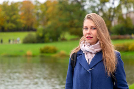 Autumn season. Portrait of a woman in a coat, against the background of an autumn Park with lakeの写真素材