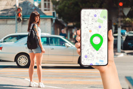 A hand holds a smartphone with an online map app and a marked destination. In the background, a...