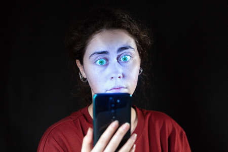 Portrait of a woman looking at her mobile phone like a zombie. Black background. Copy space. The...