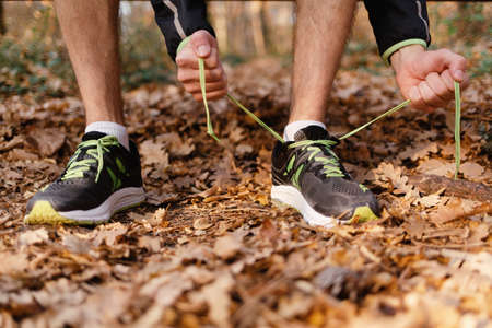 The concept of sport. A man ties his shoelaces on his sneakers. Close - up view of legs and arms.の写真素材