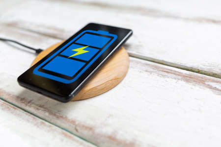 Concept of modern technologies. On the wireless charger is a black smartphone with a blue battery...