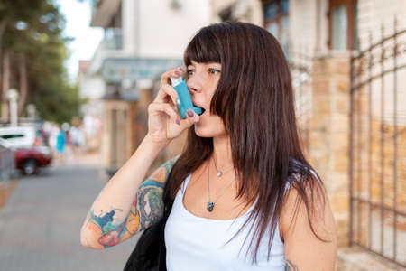 Portrait of a young woman who inhales an inhaler. There's a tattoo on my arm. Outdoor. The concept of asthma and drug dependence.の写真素材