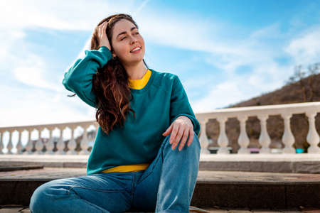 A young smiling woman in casual clothing poses against a blue sky. Copy space. Concept of new ideas, reflections and advertising.の写真素材