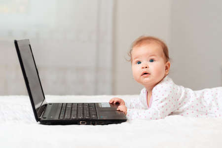 Cute baby is lying on the bed and touching the laptop. Side view. Concept of online communications.の写真素材