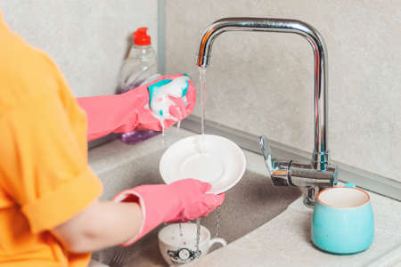 Housework. A woman in pink rubber gloves is washing dishes. View from the shoulders.