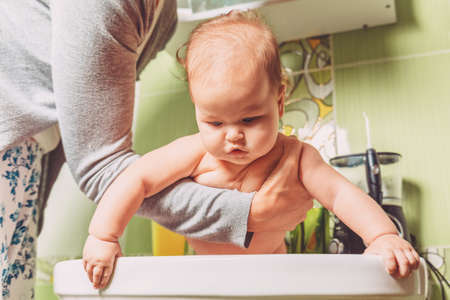 A mother holds her baby in her arms and bathes it in the sink. The concept of caring for the child.の写真素材