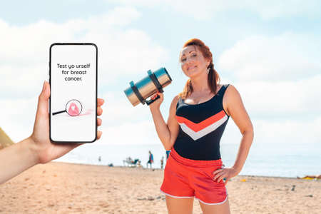 A females hand holds a smartphone with an inscription about a breast cancer test. In the background...