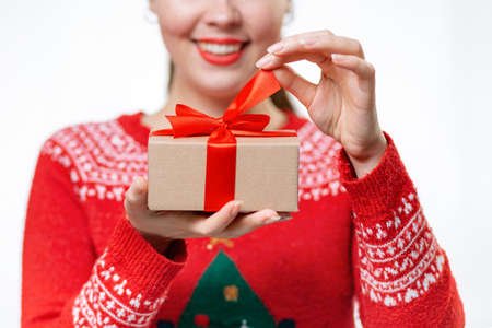 Blurred a young smiling woman in a new year's sweater holding a gift and untying a ribbon. Close up of hands. White background. The concept of Christmas shopping.の写真素材